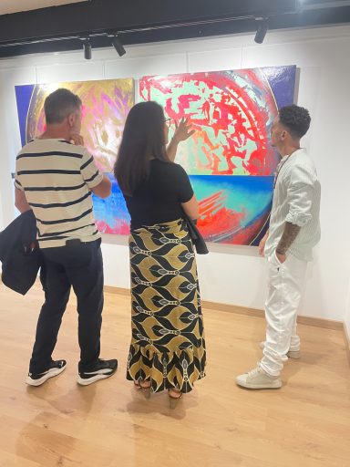 Trois personnes admirent des œuvres d'art colorées dans une galerie.