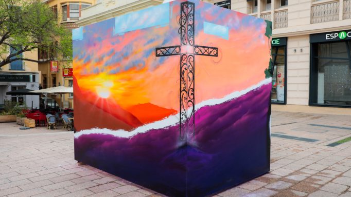 Une fresque colorée représentant une croix sur fond de coucher de soleil.
