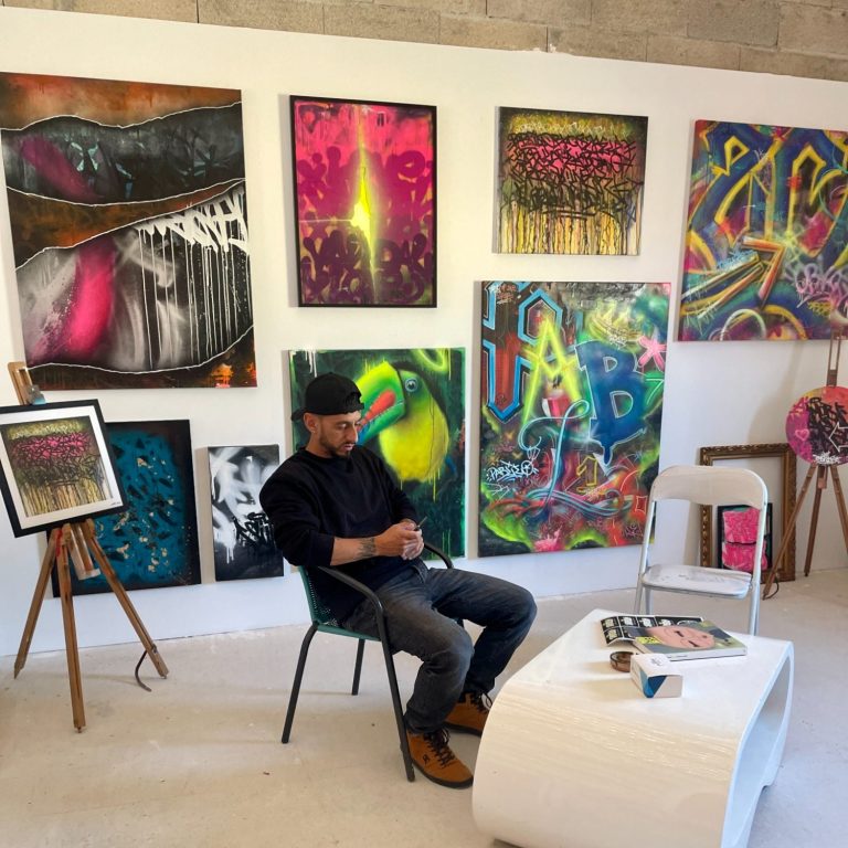 Pablito Mourer Artiste Peintre Un artiste assis dans son atelier entouré de toiles colorées de style graffiti contemporain.